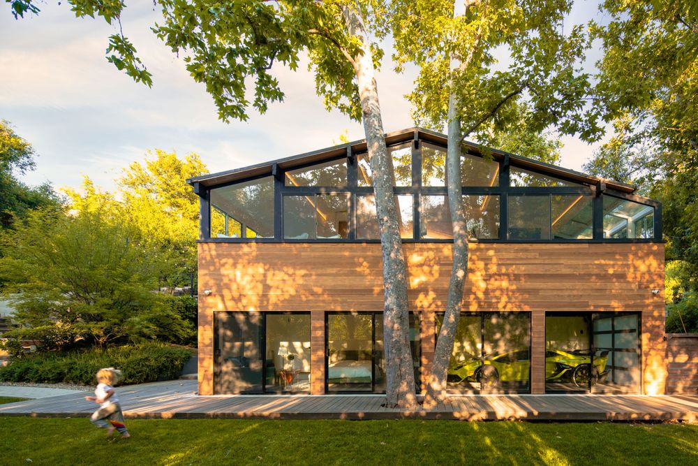 Contemporary two-story wooden house with large windows nestled among autumn trees.