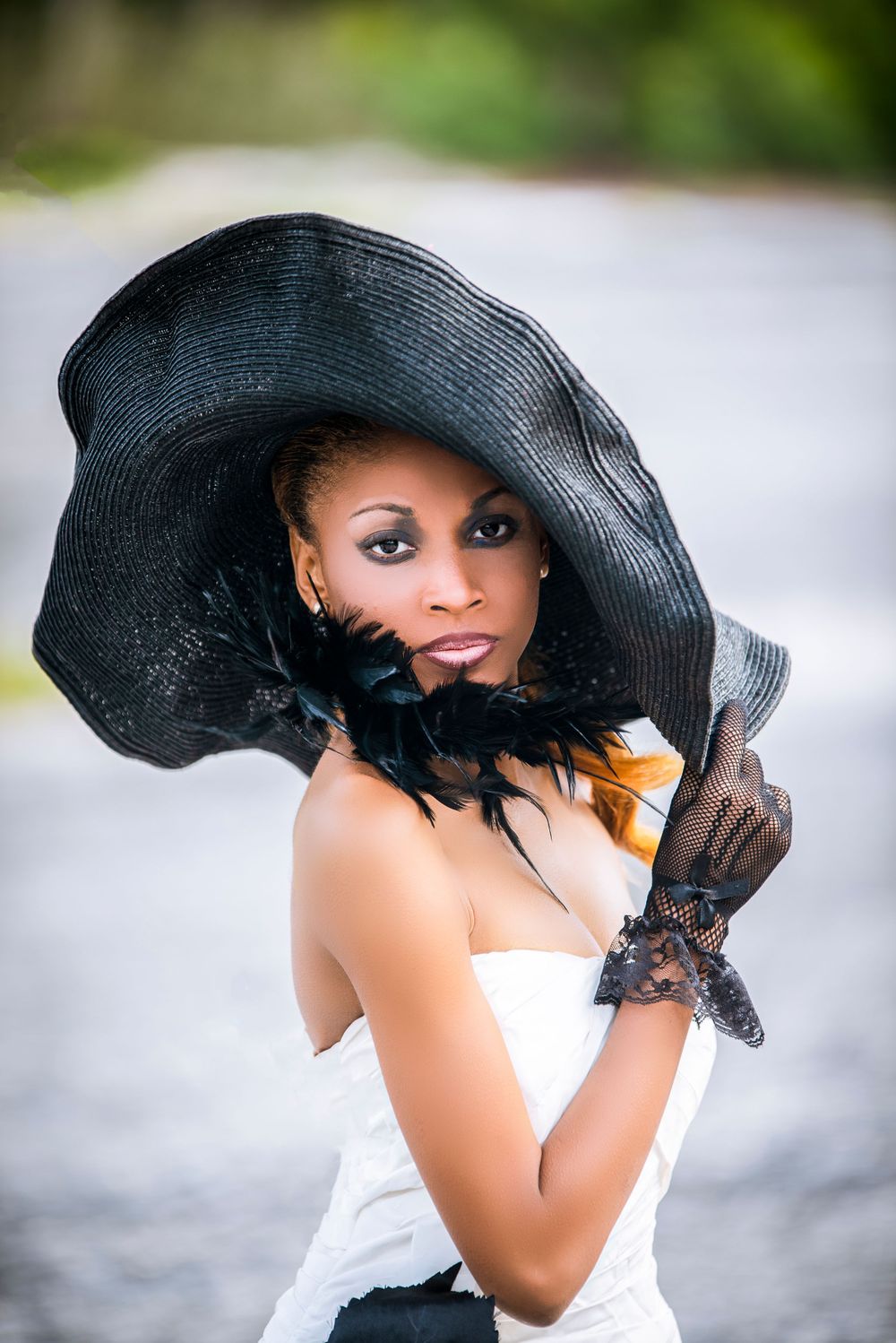 Vintage-inspired portrait with dramatic black sun hat and lace gloves in soft lighting.