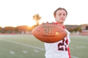 Senior boy holding Wilson football on a field at sunset for senior session in Springfield, MO.
