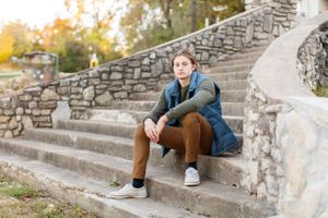 Senior boy resting on stone steps wearing denim jacket and brown pants in outdoor setting for a senior session in Springfield, MO.