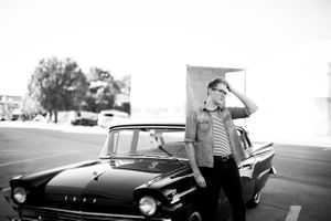 A black and white photo of a senior boy in vintage clothes standing next to a classic 1950s Ford car for a senior session in Springfield,MO.