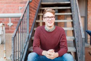 Senior boy on brick steps featuring a burgundy sweater and relaxed pose for a senior session in Springfield, MO.