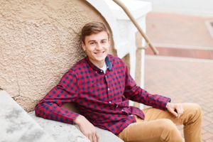 Senior boy sitting on concrete steps wearing red plaid flannel shirt and khaki pants for a senior session in Springfield, MO.