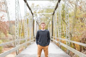Senior boy standing centered on metal bridge walkway during autumn season for a senior session in Springfield, MO.