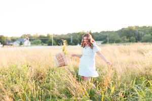 Senior girl in light blue dress holding wicker basket while standing in golden wheat field at sunset for a senior session in Springfield, MO