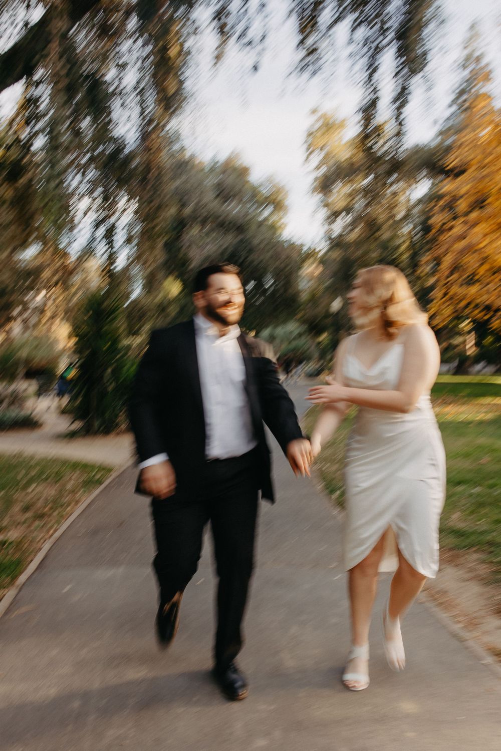 Motion-blurred photo of couple running together on autumn path in formal wear.