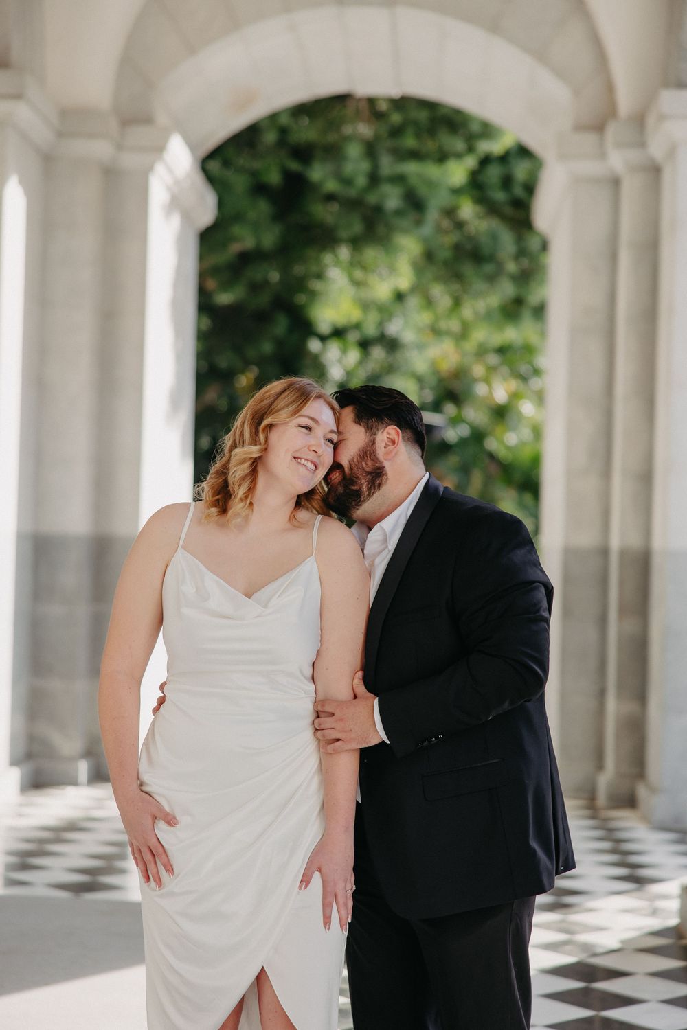 Intimate moment shared between couple in formal attire under classical arched colonnade.
