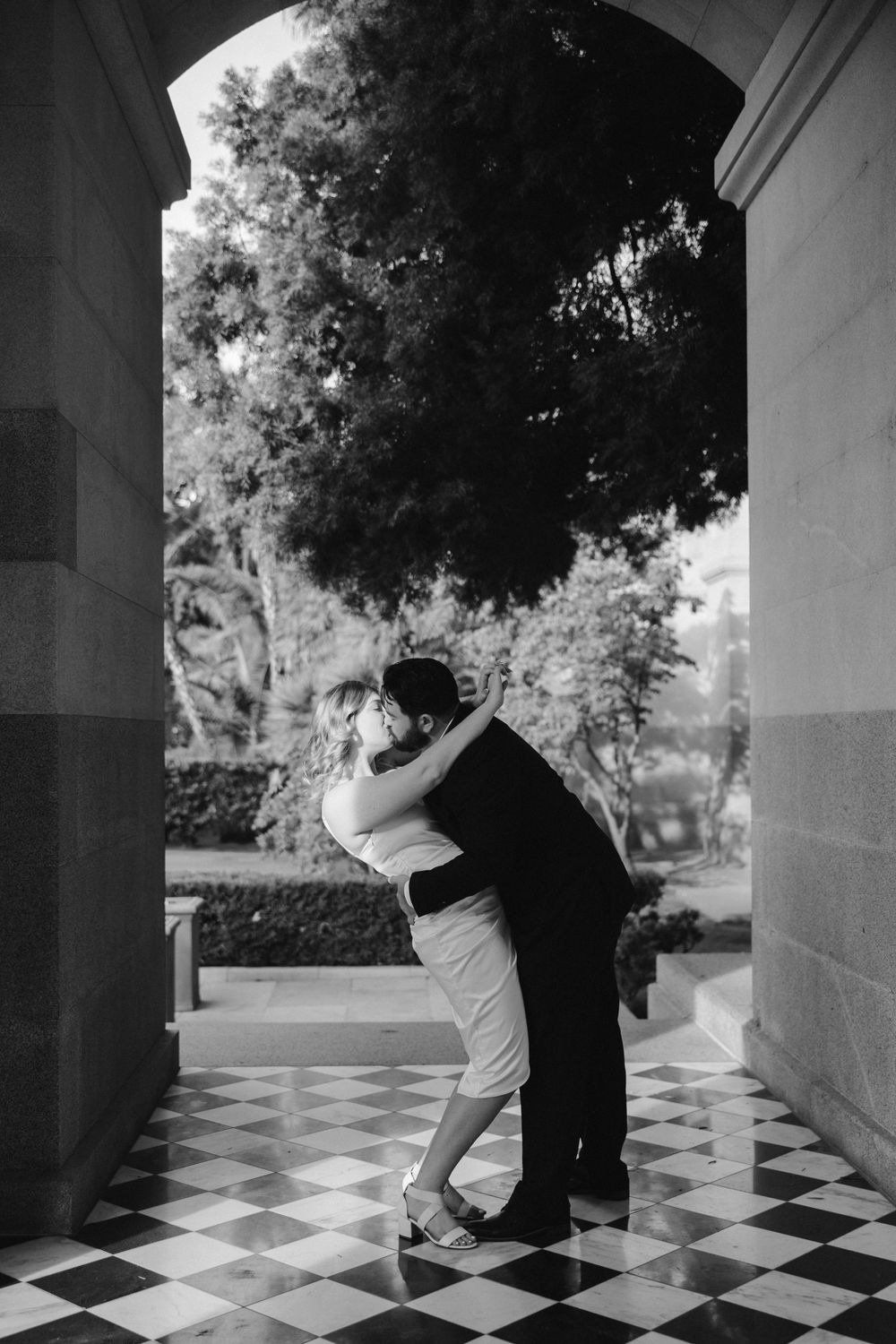 Black and white photo of couple dancing beneath architectural archway.