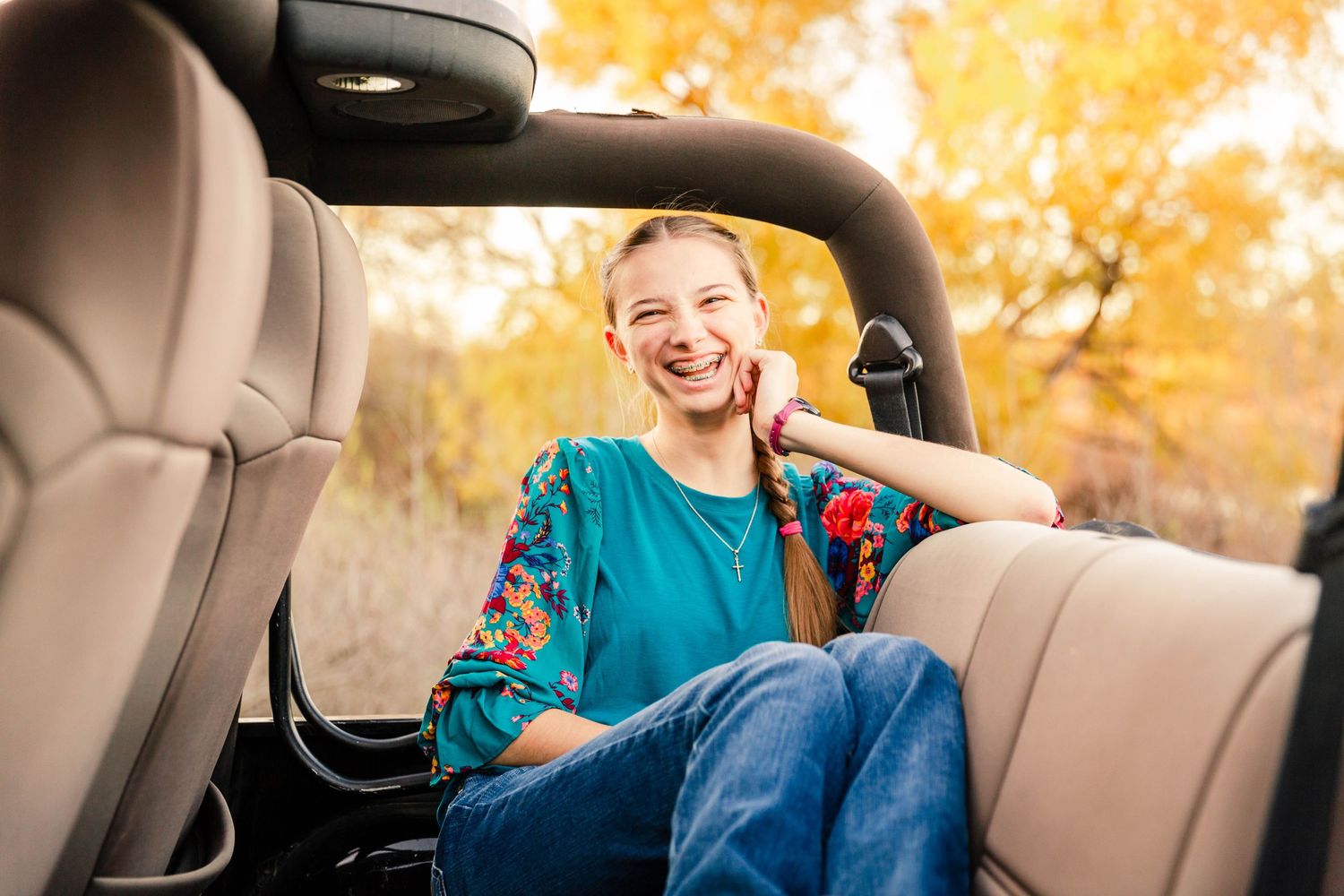 Interior of car with senior girl and autumn foliage visible through windows during sunset.