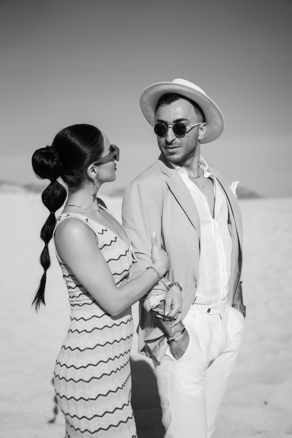 Black and white portrait of a fashionable couple in summer attire standing on sand dunes.