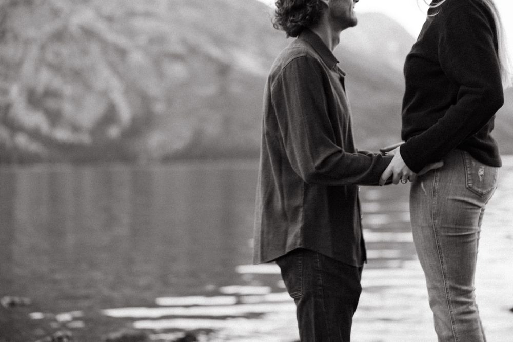 Silhouettes of couple standing by mountain lake during engagement session.