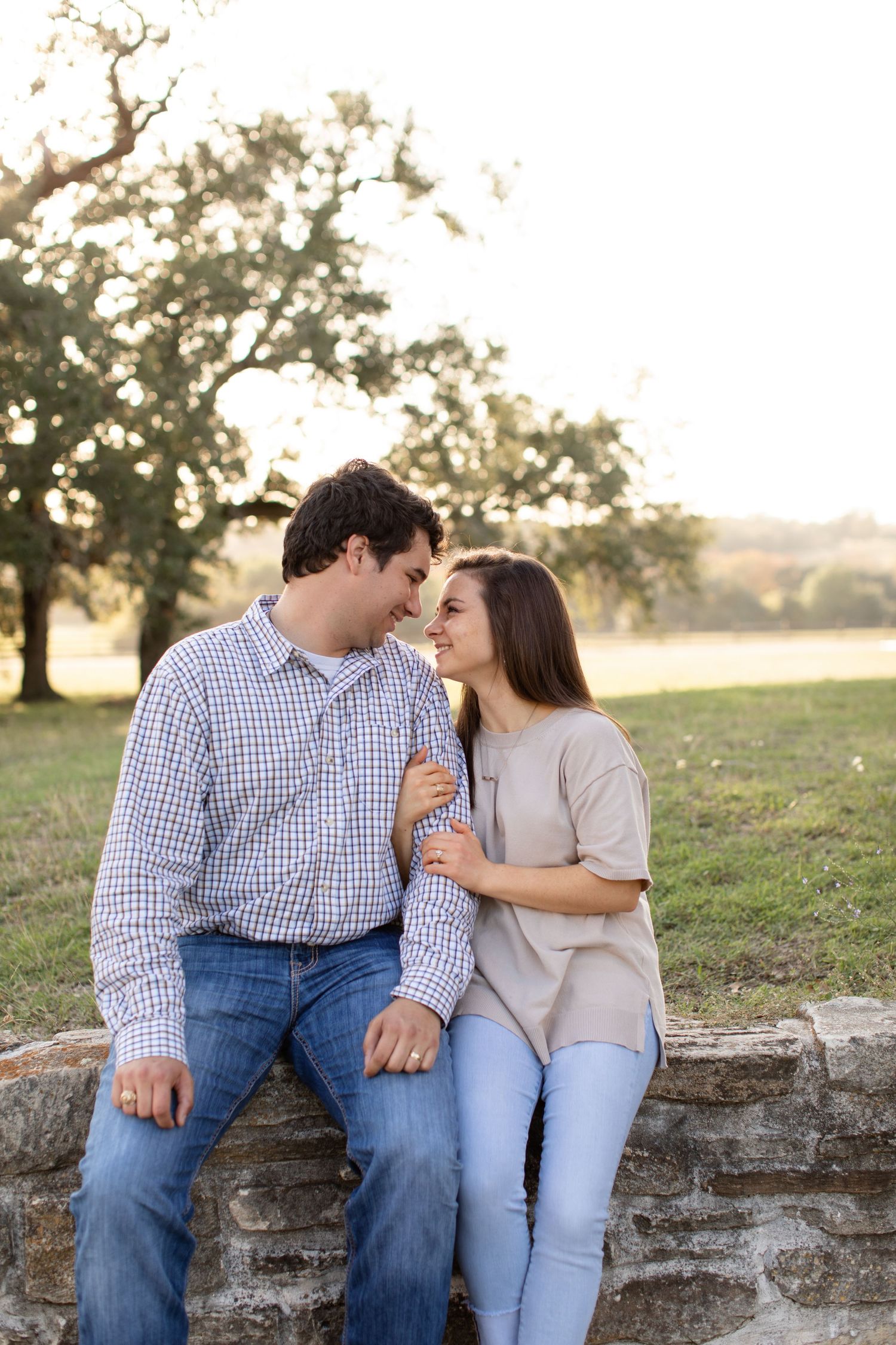 A couple shares an intimate moment while sitting on a stone wall at sunset.