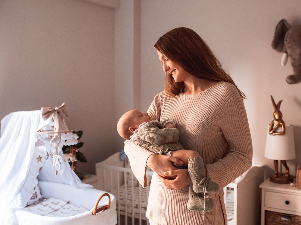 A nursery scene with someone holding a baby near a white crib with decorative accessories.