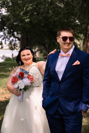 Wedding couple in navy suit and white dress poses outdoors with coral and silver bouquet.