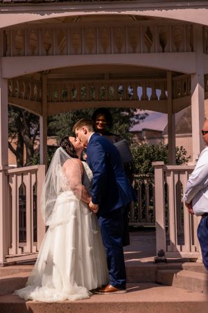 Wedding couple shares intimate moments under white gazebo during ceremony.