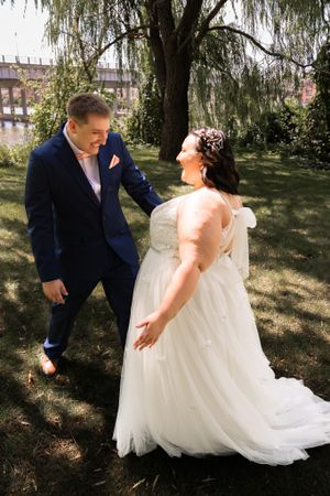Newlyweds share candid moments during outdoor wedding photoshoot under trees.