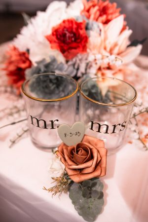 Mr and Mrs drinking glasses surrounded by coral roses and floral arrangements.