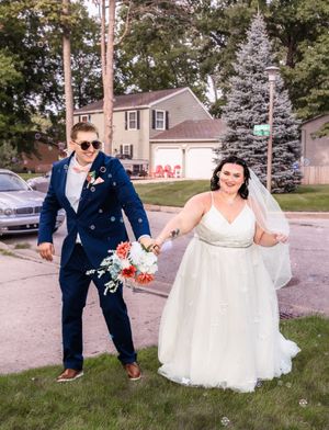 A joyful couple poses on their wedding day in front of a suburban house.