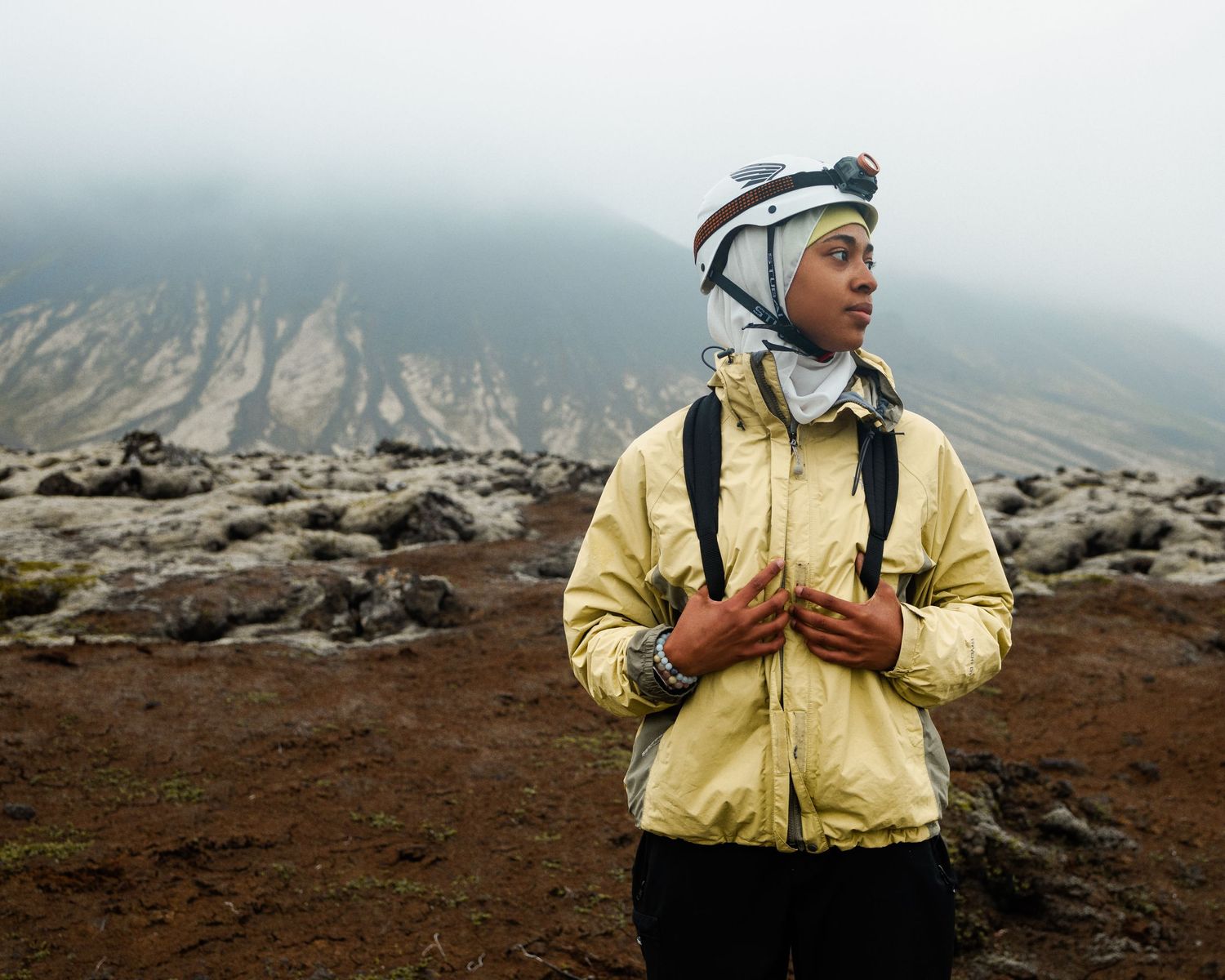 Hiker in yellow jacket explores misty volcanic terrain.