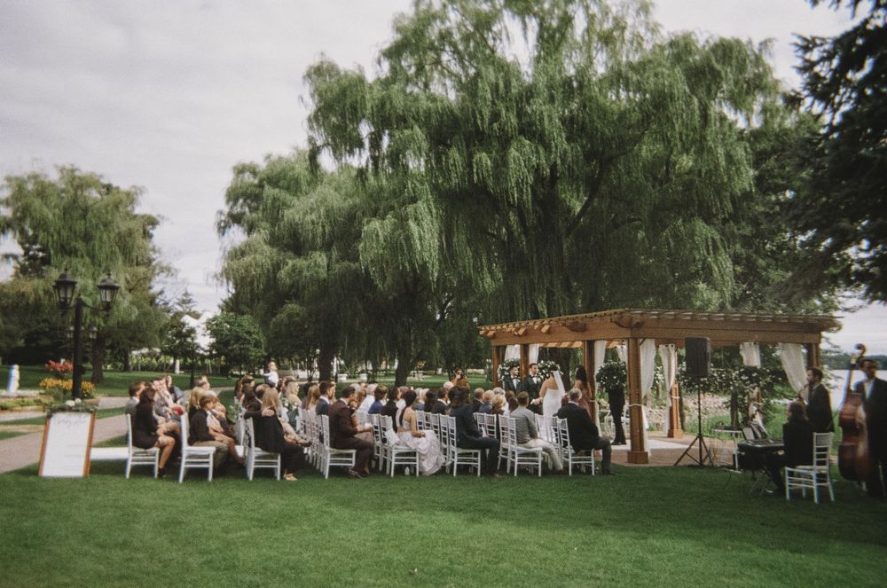Outdoor wedding ceremony setup with white chairs under weeping willow trees.