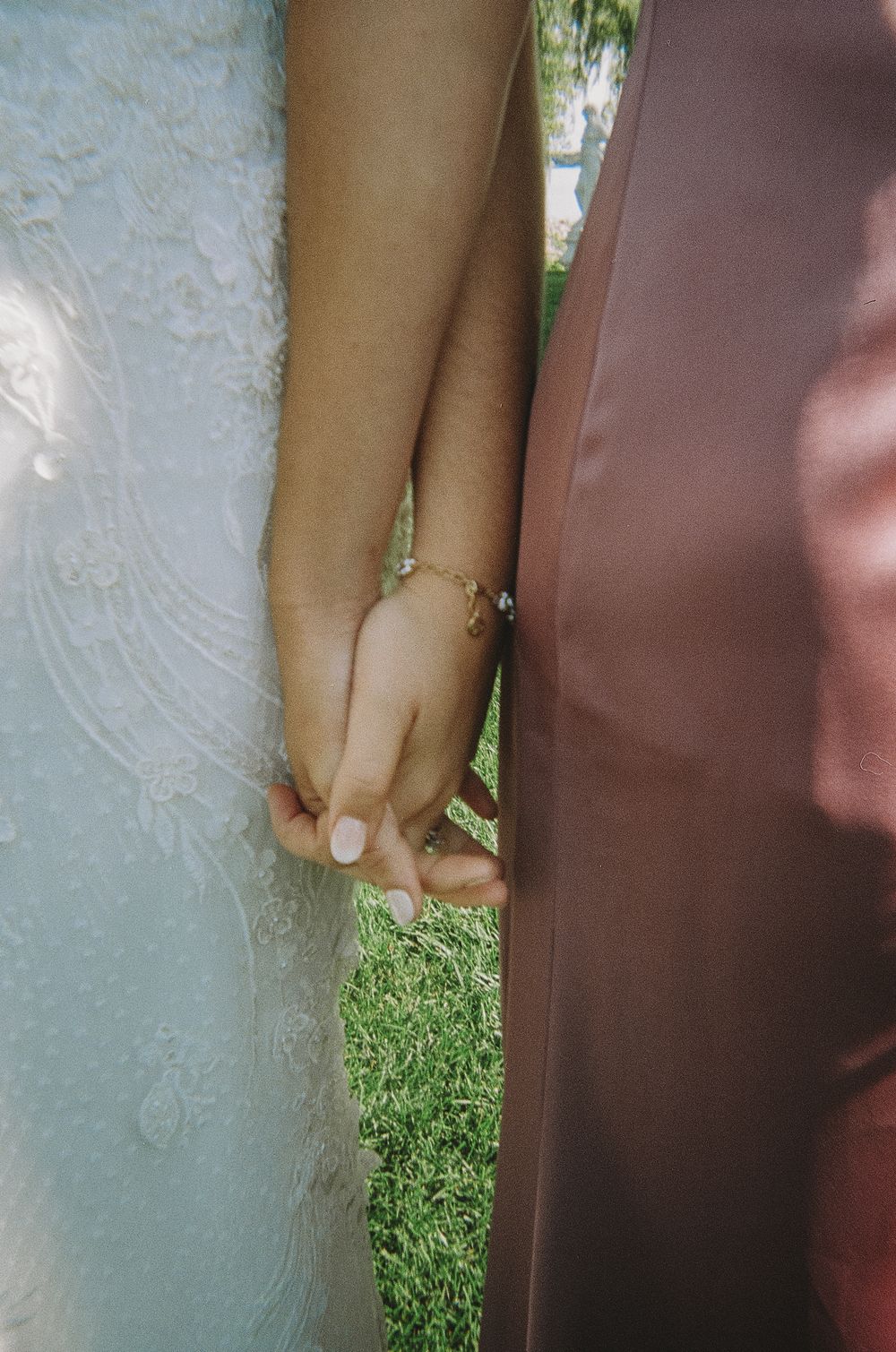 Close-up of joined hands with wedding rings against a lace dress and suit.