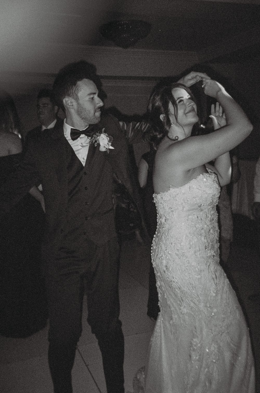 A couple energetically dances together at their wedding reception in black and white.