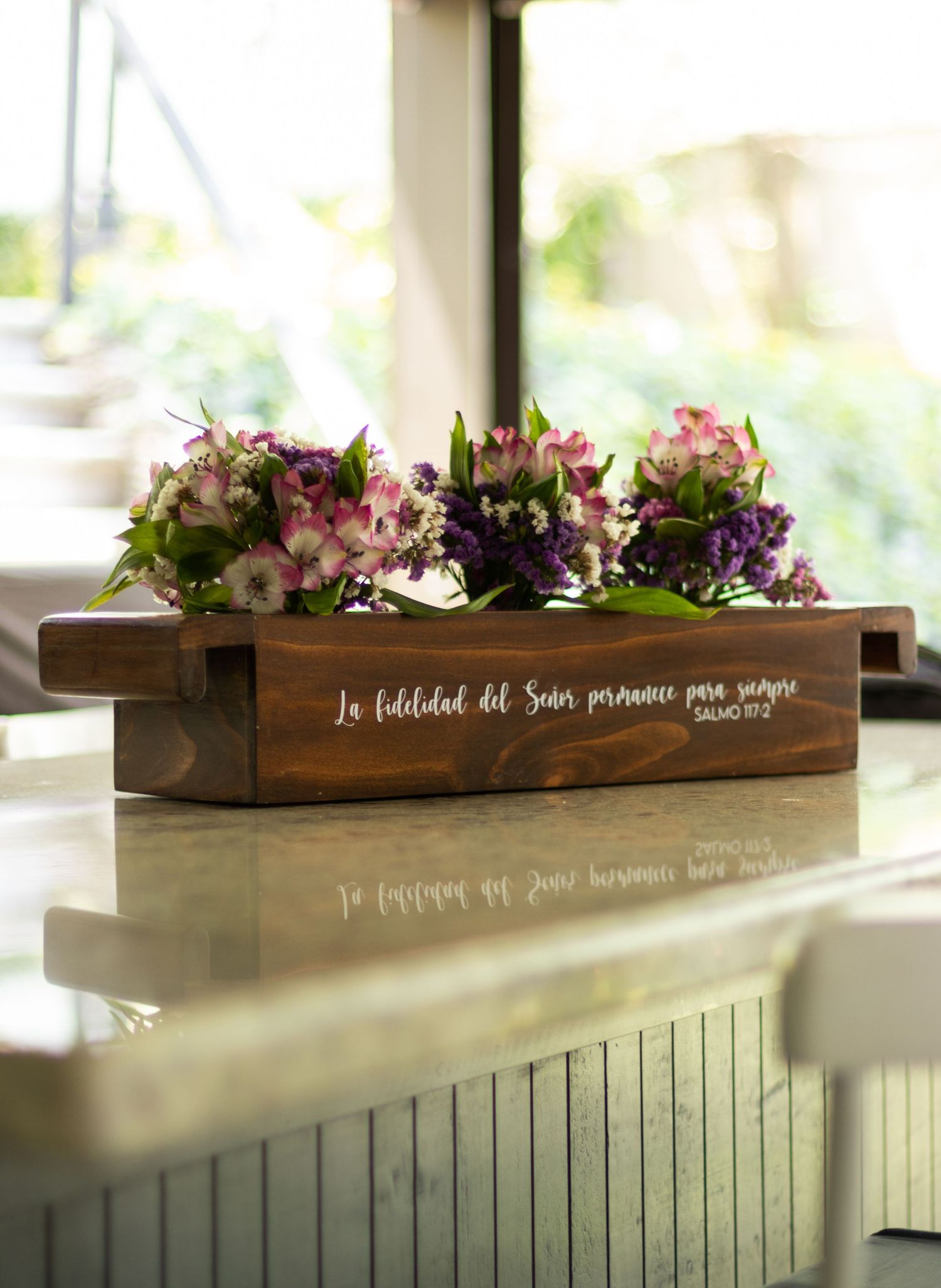Wooden box centerpiece filled with pink and purple flowers displayed on a windowsill.