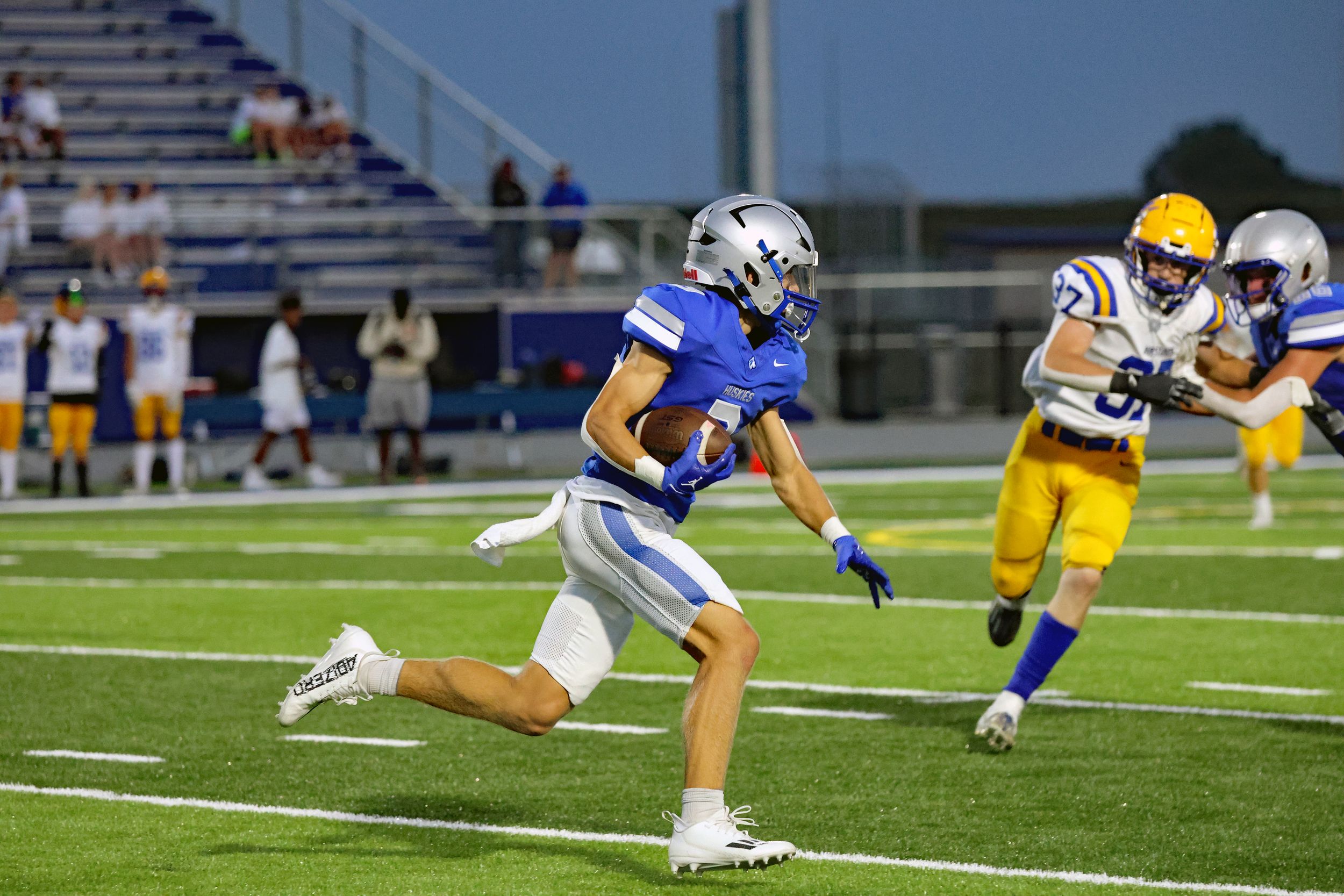 Football player running with ball during game against yellow-uniformed opponents.