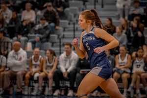 A basketball player in blue Owatonna uniform runs down court during an intense game moment.