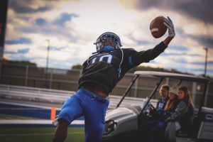 Player making dramatic one-handed catch during football game at sunset.