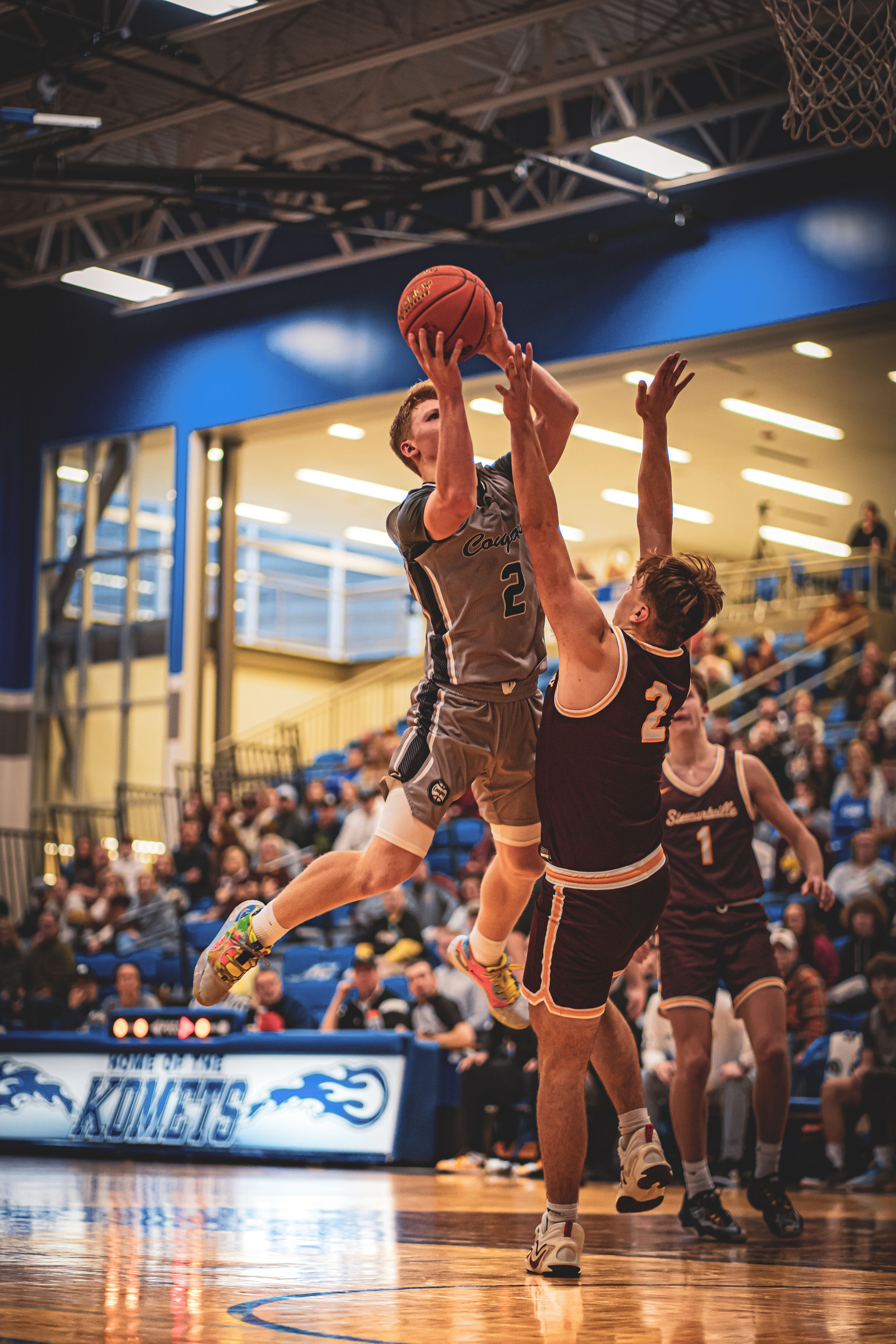 Basketball player leaping for a shot during competitive game on indoor court.