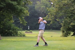 Golfer in light colored clothing taking a swing on a lush green course.