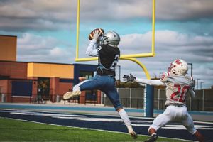 Football players competing for catch in endzone during competitive game.