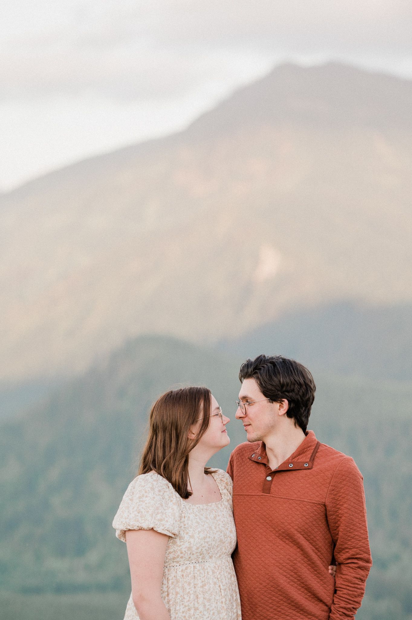 A couple shares a romantic moment against a backdrop of misty mountains during sunset.