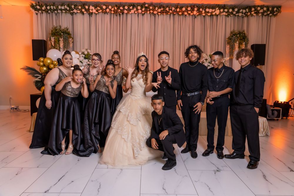 Wedding party members strike fun poses during formal group photo in decorated reception venue.
