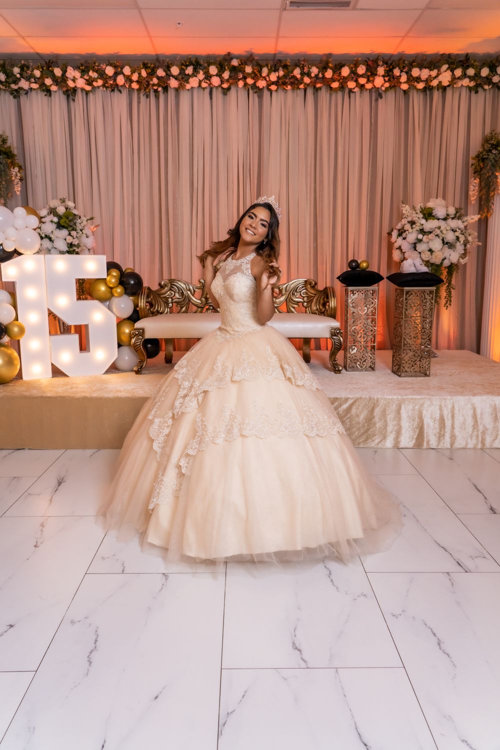 Bride in champagne ballgown poses by illuminated numbers and floral decorations.