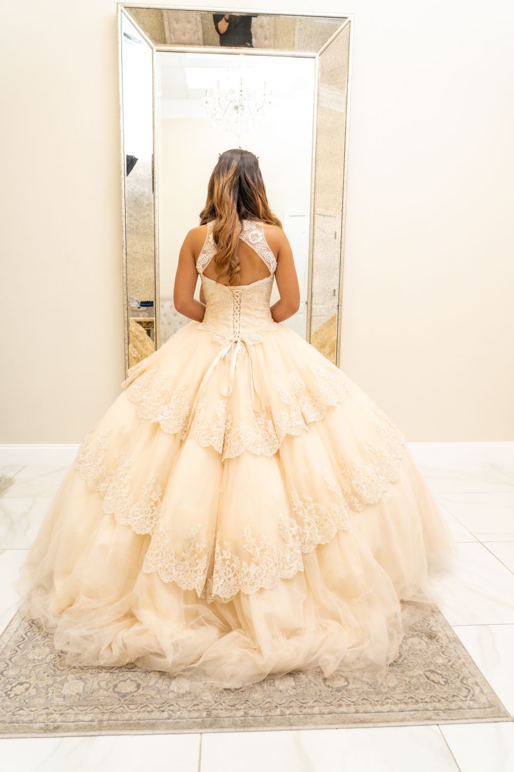 Back view of a champagne-colored ball gown with tiered lace details reflected in a large mirror.