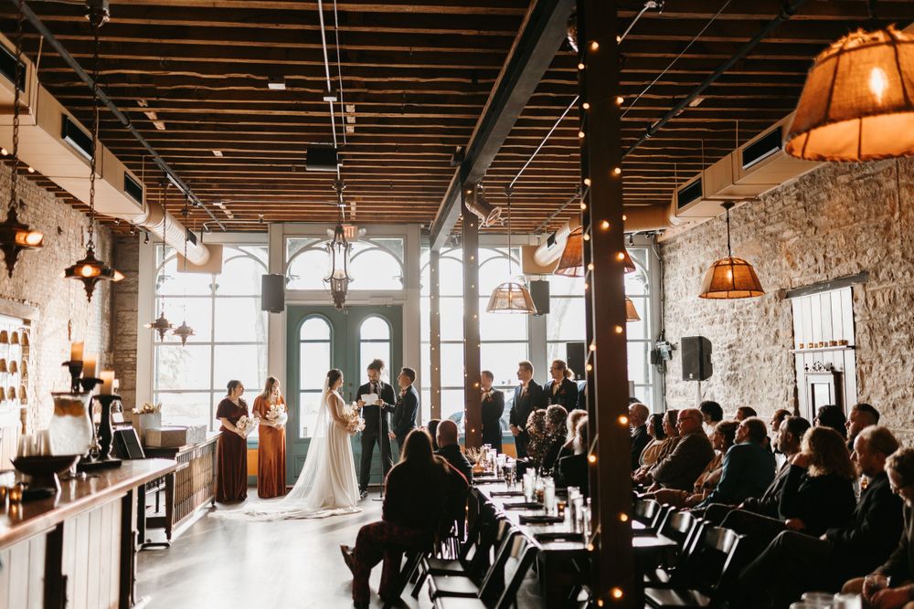 Wide angle view of intimate indoor wedding ceremony with guests seated in rustic industrial venue.