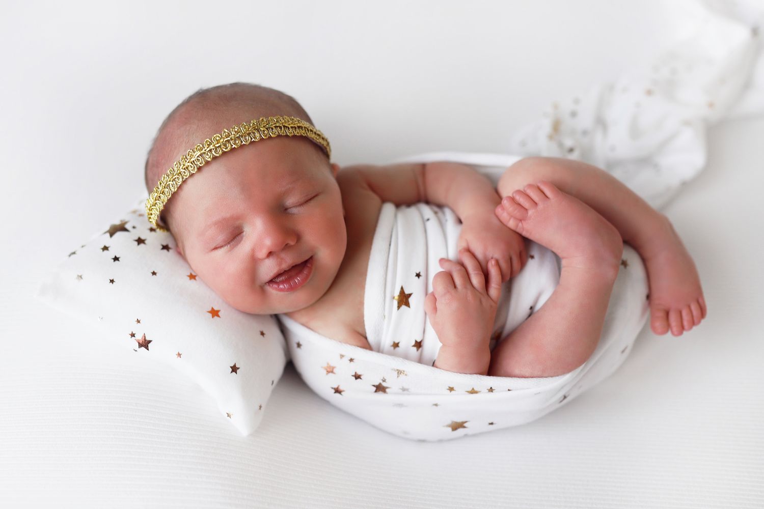 Peaceful sleeping newborn in star-patterned white outfit with gold headband.