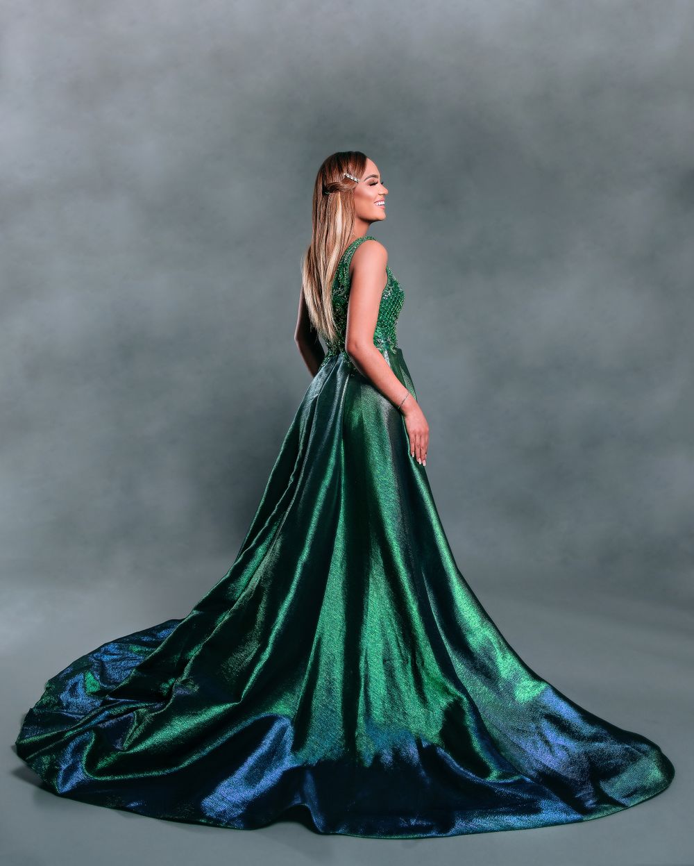 Elegant emerald green ballgown with dramatic train photographed against grey background.
