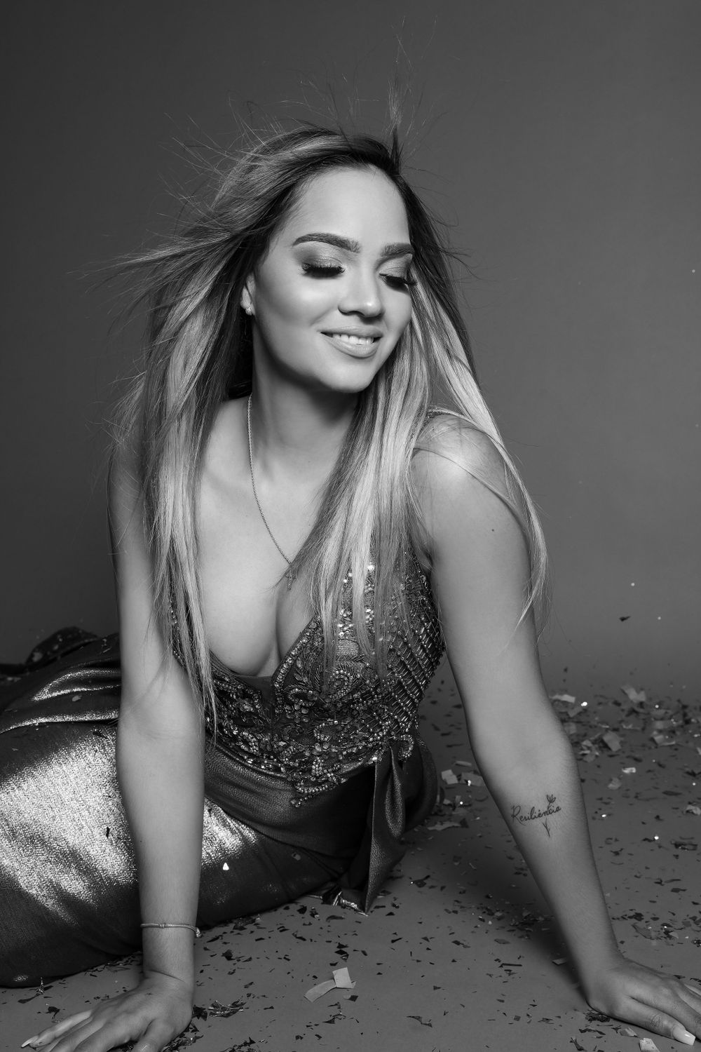Black and white glamour portrait with sparkly dress and windswept hair against dark background.