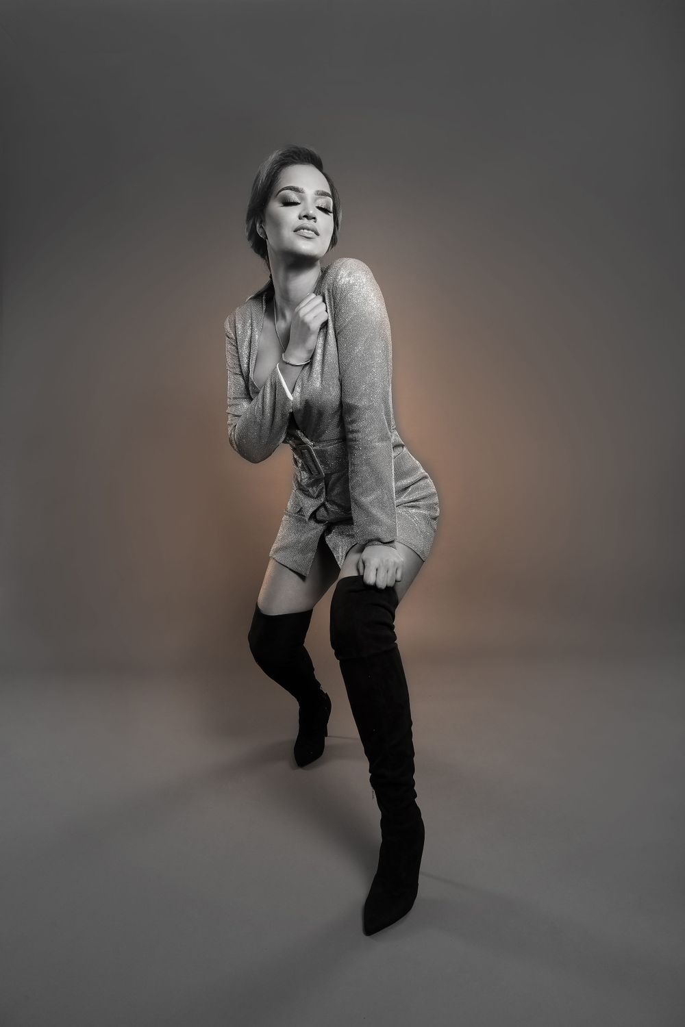 Fashion portrait in grey sweater and thigh-high boots against neutral studio backdrop.