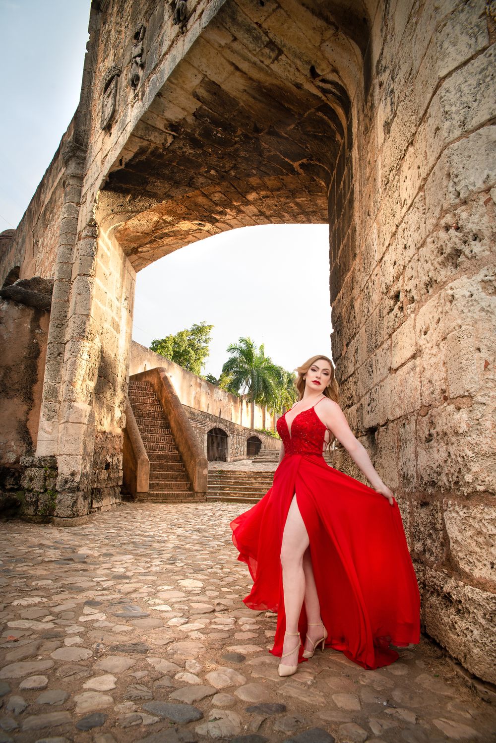 Flowing red dress photograph in historic stone archway with tropical palm trees in background.