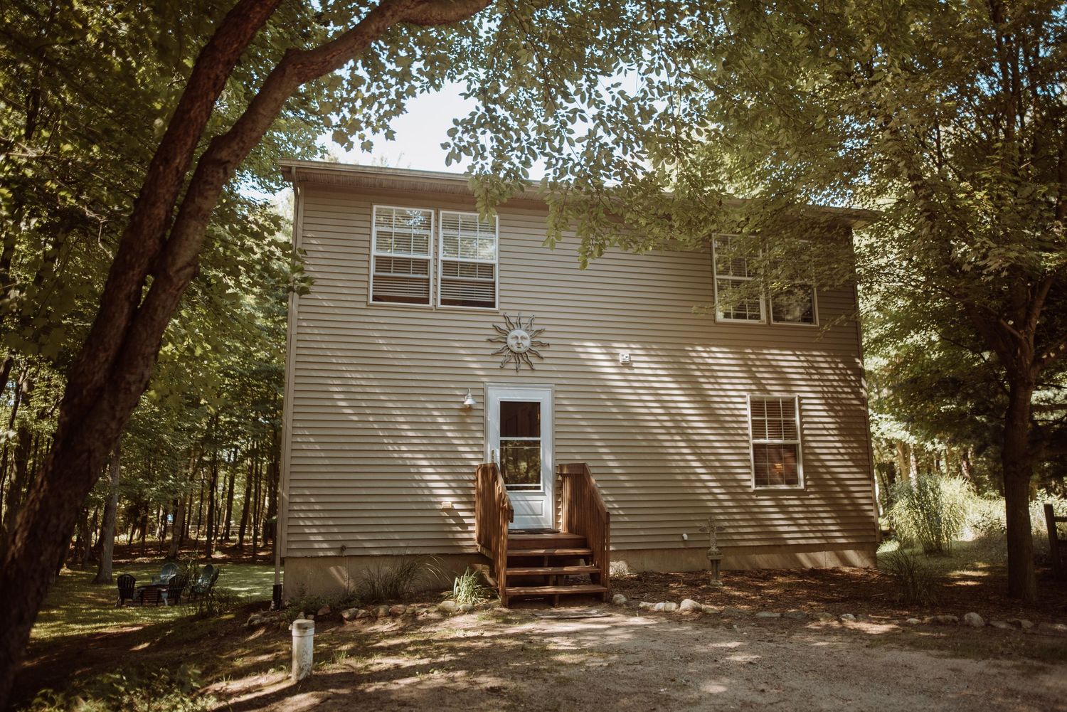 Two-story beige residential house with white trim nestled among trees in a wooded setting.