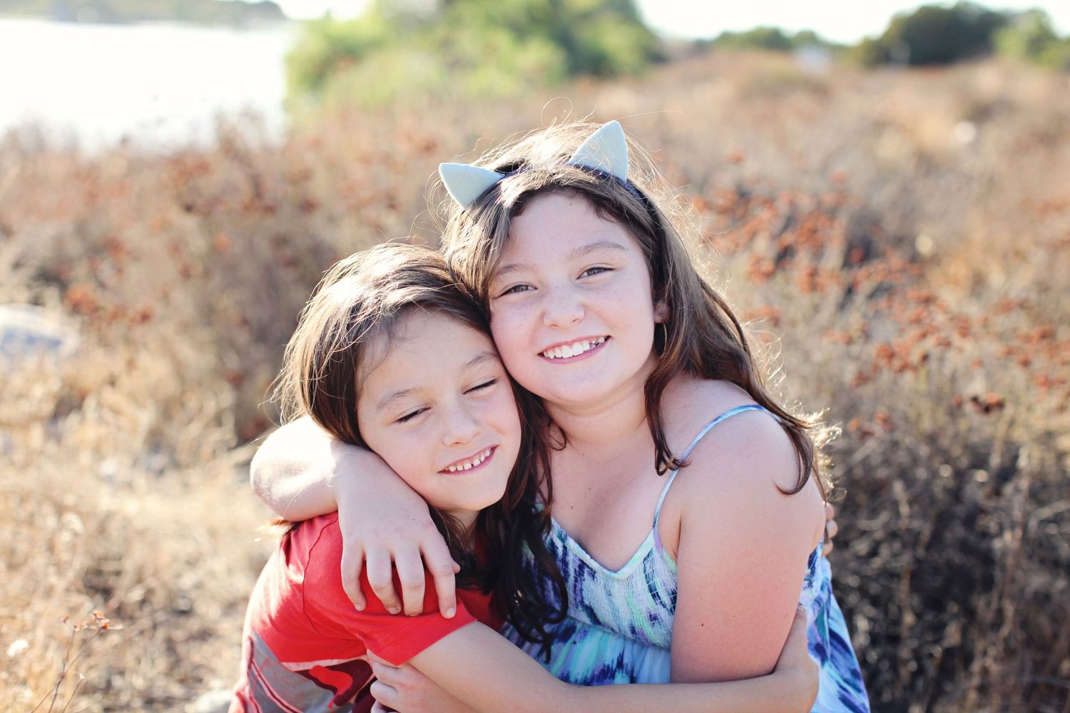 Two children hugging and smiling outdoors in natural setting.