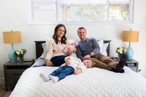 Family relaxes together on white bed with matching decor and window lighting.