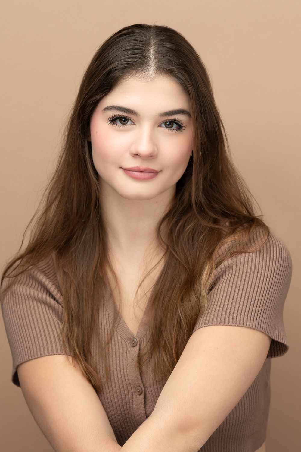 Warm portrait in ribbed brown top with long flowing hair against beige background.