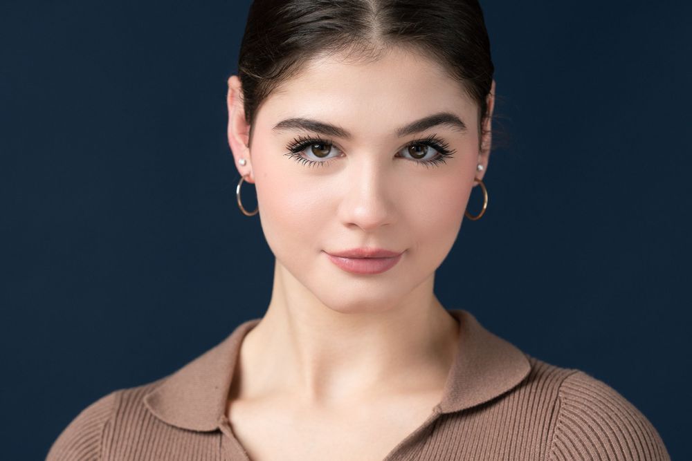 Close-up portrait in brown collared top with hoop earrings against dark background.
