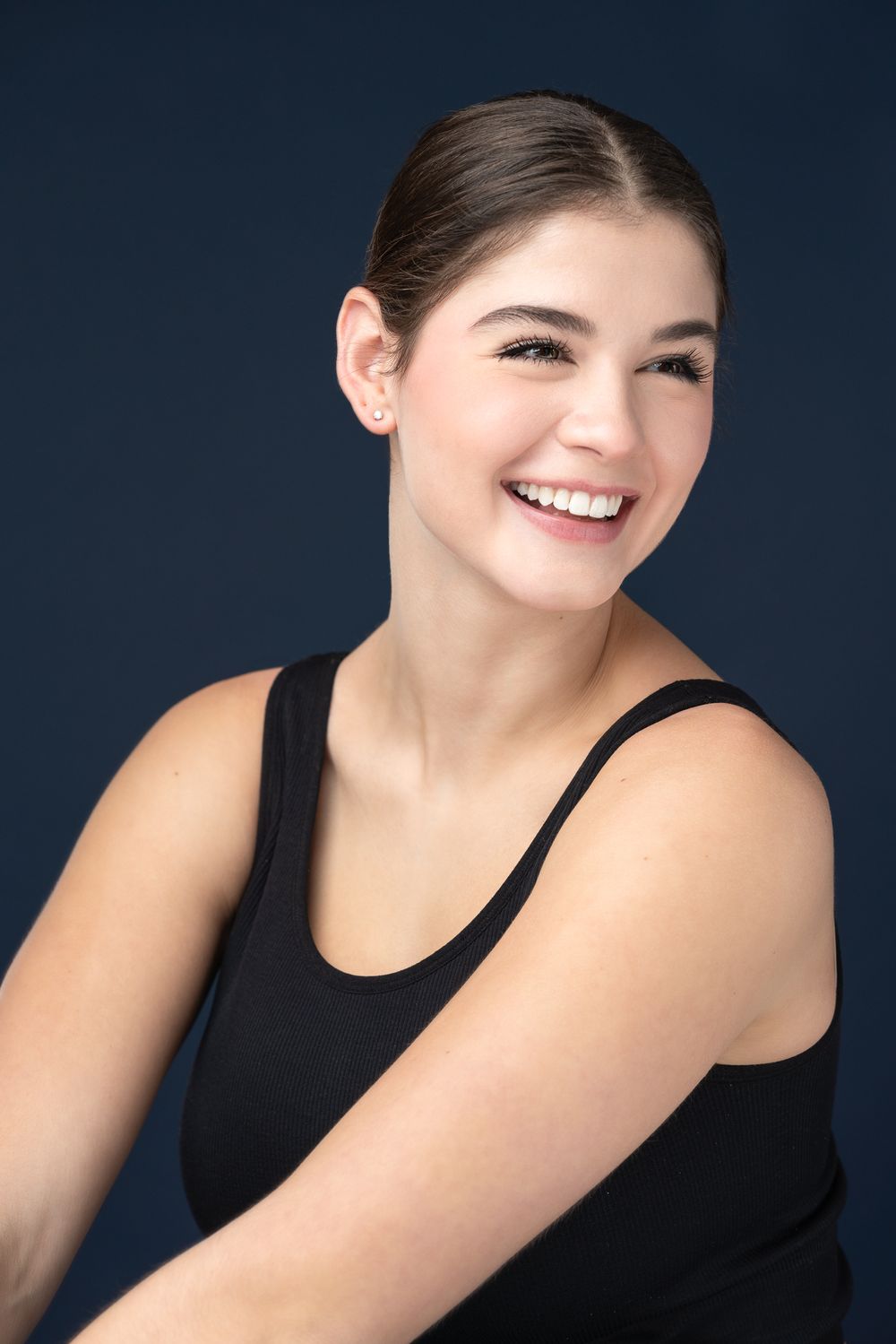 Casual studio portrait in black tank top with natural smile against navy background.