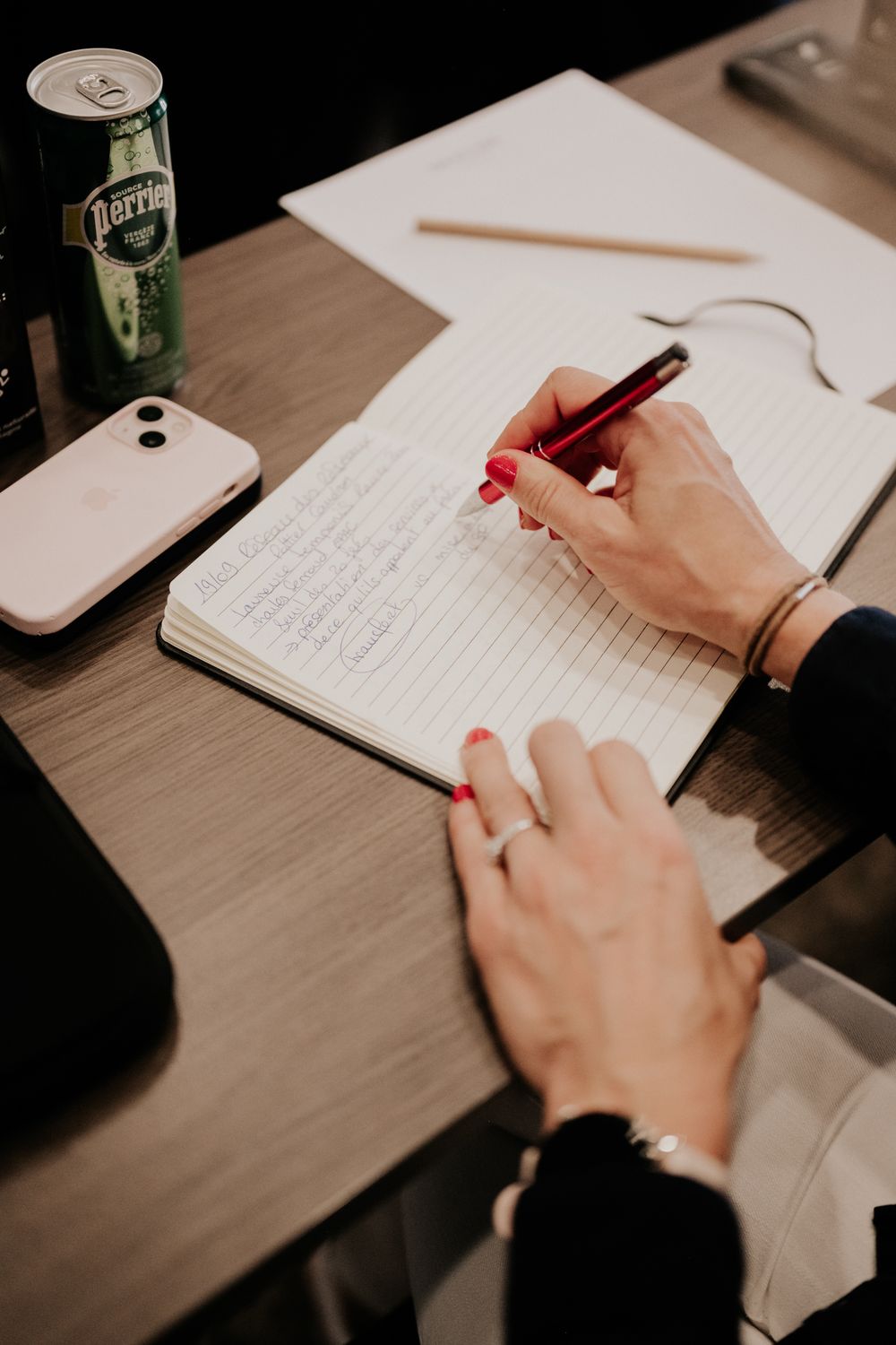 Close-up of hands writing notes in a notebook on a wooden table.